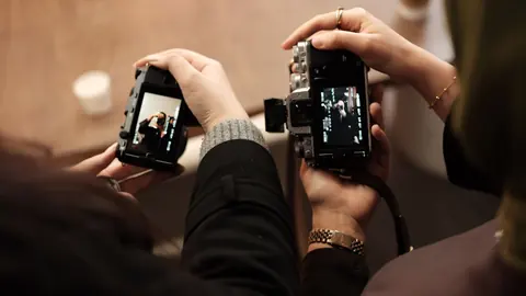 Two people holding cameras, comparing photos side by side on the screens