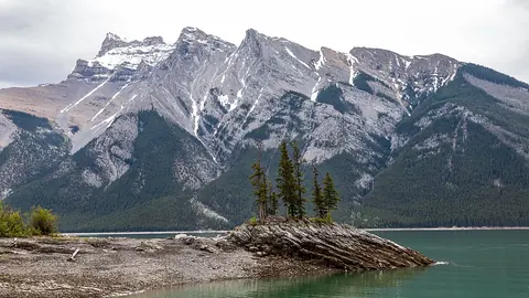 Turquoise Lake Minnewanka with rocky pine-covered peninsula below snowy peaks