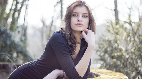 Natural-light outdoor portrait of an adult woman resting her chin on her hand, both eyes open and sharp