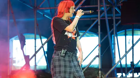 Singer on stage under blue scaffolding lighting with orange flame effects at the edges