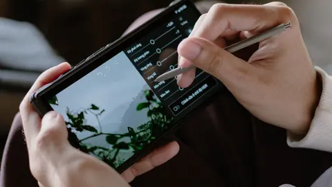 Hand using a stylus to adjust exposure sliders while editing a photo on a phone