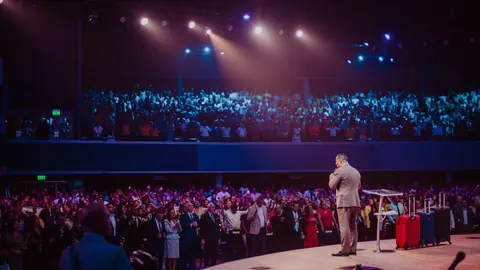 Speaker on a large conference stage lit by warm and blue stage lights