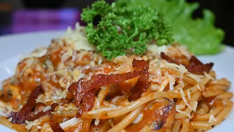 Close-up of a plated spaghetti dish with bacon, cheese and parsley garnish