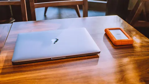 Laptop beside a rugged orange external hard drive on a wooden table