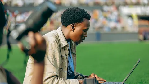 Press photographer working on a laptop pitch-side at a stadium
