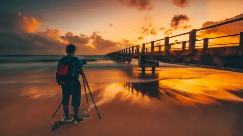 Landscape photographer at a tripod shooting a pier at sunset