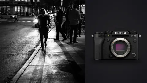Fujifilm X-T5 product photo beside man walking a lit sidewalk past pedestrians at night