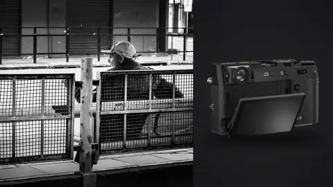 Fujifilm X100VI product photo beside man in a flat cap sitting behind a metal fence