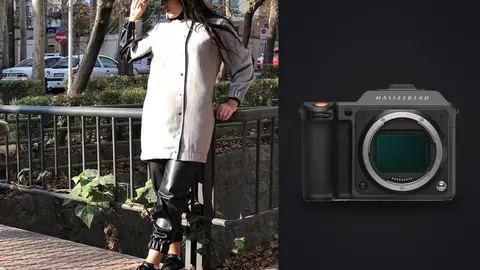 Hasselblad X2D 100C product photo beside person in a white trench coat and leggings by an iron fence