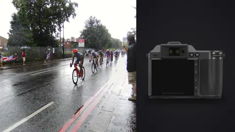 Hasselblad X2D 100C product photo beside cyclists racing through heavy rain past umbrella-holding spectators