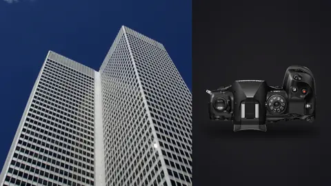 OM System OM-1 Mark II product photo beside twin white skyscrapers converging against a deep blue sky