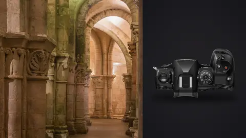 OM System OM-1 Mark II product photo beside atmospheric romanesque stone crypt with carved column capitals
