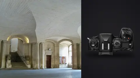 OM System OM-1 Mark II product photo beside elegant vaulted stone hall with staircase