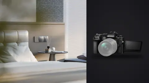 OM System OM-1 Mark II product photo beside empty bed corner with pillow and side table