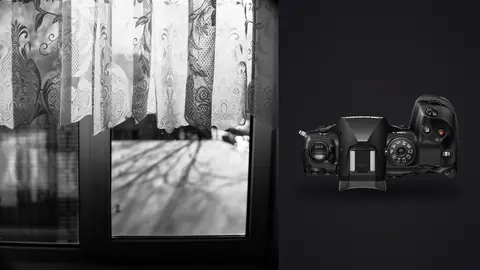 OM System OM-1 Mark II product photo beside black and white lace curtain filling window