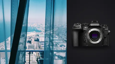 OM System OM-1 Mark II product photo beside sheer curtain with high-rise city view beyond
