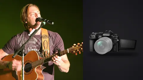 OM System OM-1 Mark II product photo beside guitarist singing on stage under green light