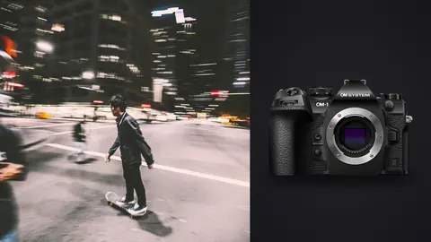 OM System OM-1 Mark II product photo beside skateboarder riding through a city street at night