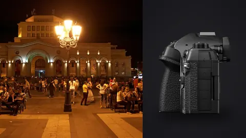 OM System OM-1 Mark II product photo beside crowd gathered in a lit historic plaza at night