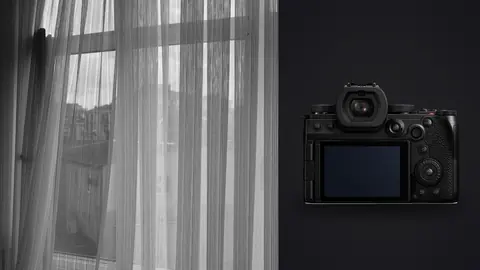 Panasonic Lumix S5IIX product photo beside grayscale sheer curtain with building view beyond