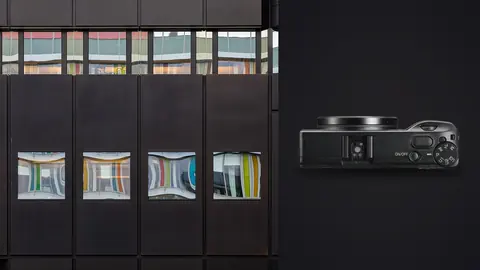 Ricoh GR IIIx product photo beside modern dark facade with colorful reflections in windows