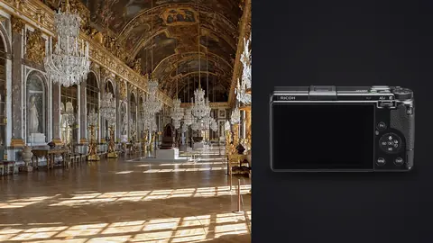 Ricoh GR IIIx product photo beside opulent gilded gallery hall with chandeliers and mirrors