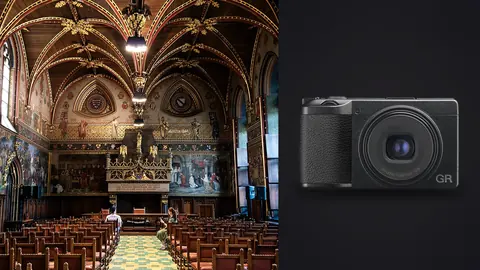 Ricoh GR IIIx product photo beside ornate gothic hall with painted murals and rows of chairs