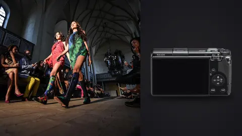 Ricoh GR IIIx product photo beside two models in colorful outfits walking a runway inside a church