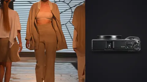 Ricoh GR IIIx product photo beside models in flowing tan and orange draped outfits on a runway