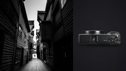 Ricoh GR IIIx product photo beside figure walking a narrow lane between wooden buildings