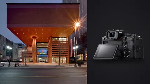 Sony Alpha 1 product photo beside modern museum building with cantilevered orange facade at dusk