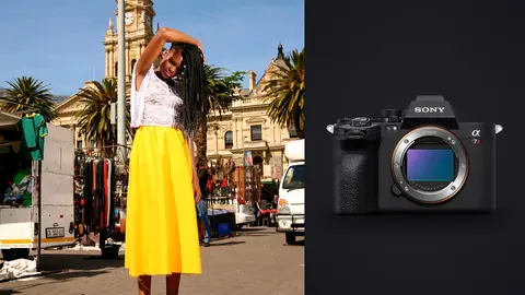 Sony a7R V product photo beside woman in a white top and yellow skirt poses near a clock tower