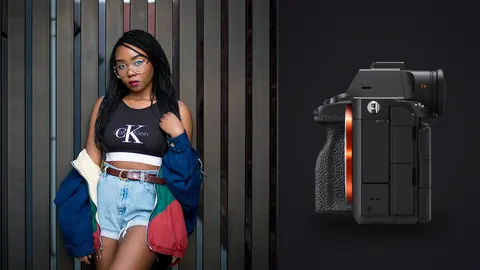 Sony a7R V product photo beside woman in a cropped top and denim shorts leans against a wall
