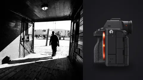 Sony a7R V product photo beside silhouetted figure walking from a dark passage into a plaza