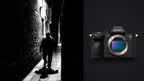Sony a7R V product photo beside silhouetted man walking down a narrow lit night alley
