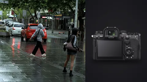 Sony a9 III product photo beside two people crossing a rainy city street past parked cars