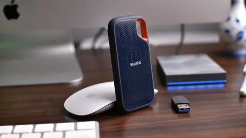 Two external storage drives and a USB stick on a desk beside an iMac