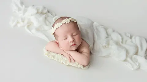 Newborn sleeping on a knit pillow wrapped in white, studio lighting