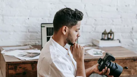 Photographer thoughtfully reviewing an image on his camera at a desk
