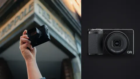 Ricoh GR IV product photo beside hand holding a compact camera up against a street building facade