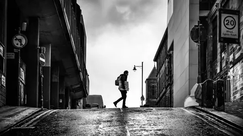 Silhouette of a man crossing a steep hillside street between buildings