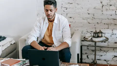 Traveler editing photos on a laptop on a couch with a camera and prints nearby