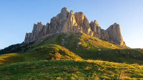 Jagged rocky mountain ridge lit gold above a grassy hillside