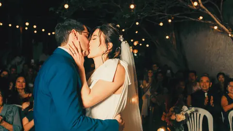 Bride and groom kissing at the altar under string lights with guests watching