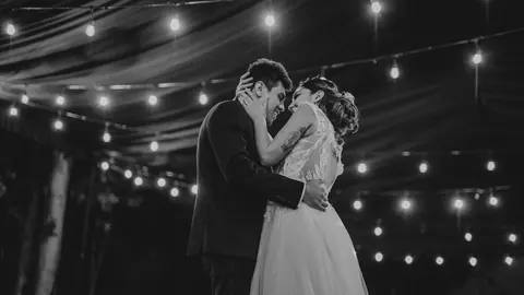 Bride and groom in an intimate embrace under string lights, black and white